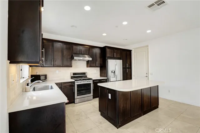 a large kitchen with stainless steel appliances a sink a stove and a refrigerator with wooden floor