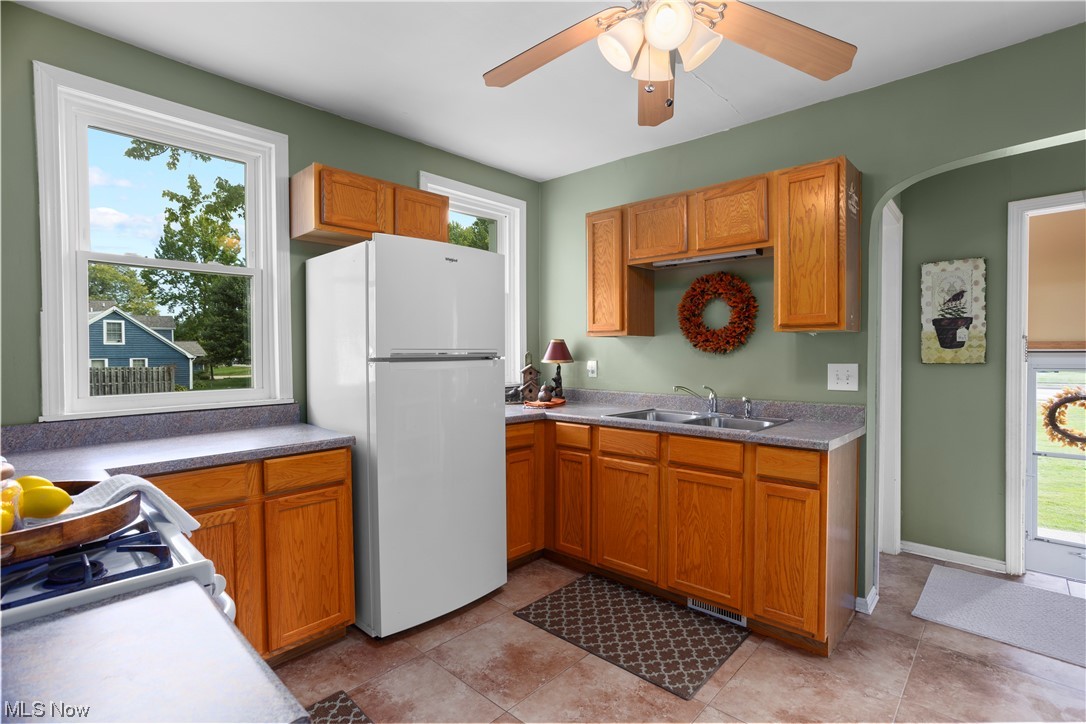 Kitchen featuring white refrigerator, tile floors, ceiling fan, and brown cabinets