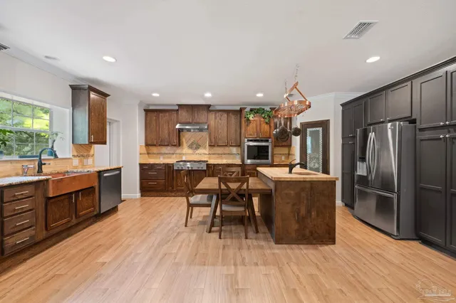 a kitchen with stainless steel appliances kitchen island granite countertop a refrigerator a stove a sink dishwasher and a dining table with wooden floor