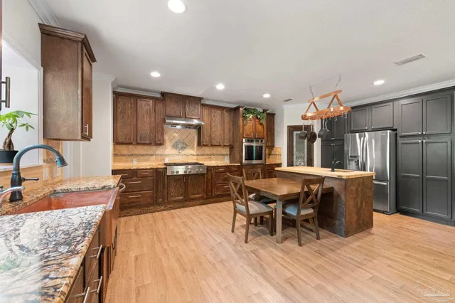 a kitchen with stainless steel appliances granite countertop a refrigerator a sink a stove and a wooden cabinets