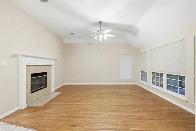 a view of an empty room with wooden floor fireplace and a window