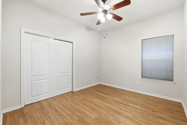 an empty room with wooden floor fan and windows