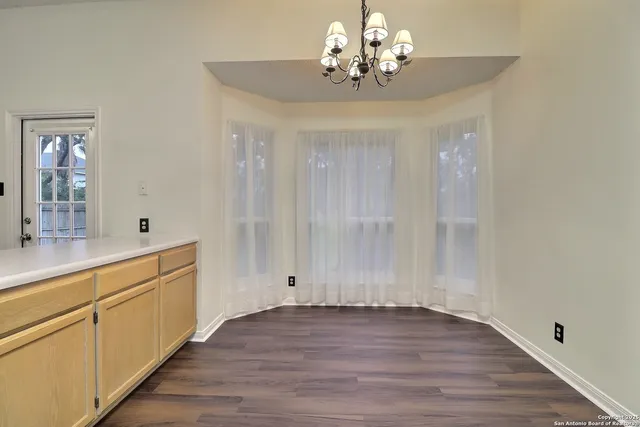 a view of an empty room with wooden floor and a kitchen