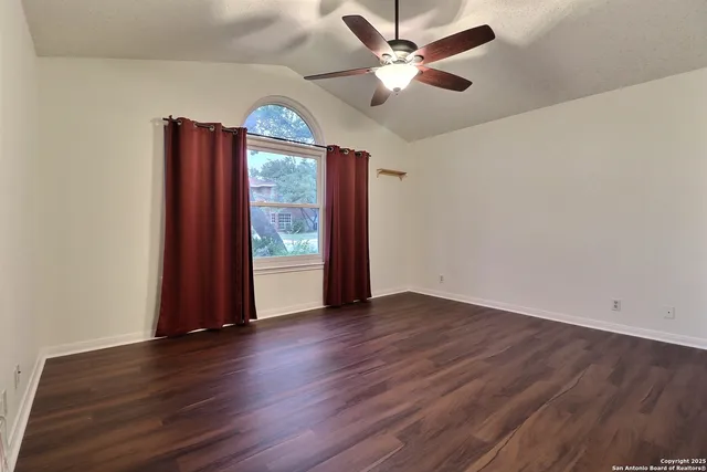 an empty room with wooden floor chandelier fan and windows