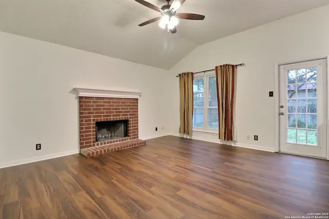 a view of an empty room with wooden floor fireplace and a window