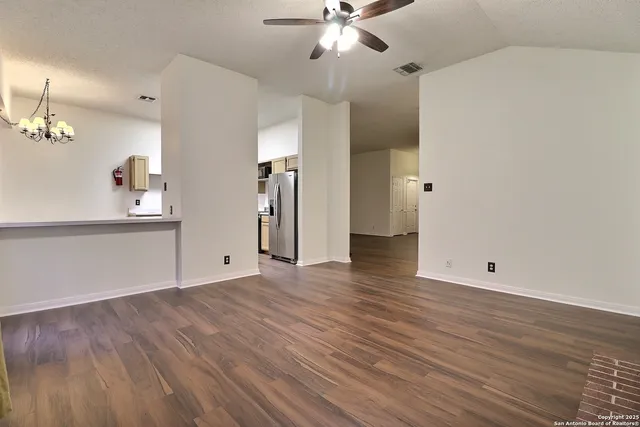 a view of an empty room with wooden floor and a ceiling fan