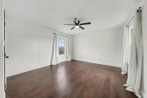 an empty room with wooden floor ceiling fan and windows