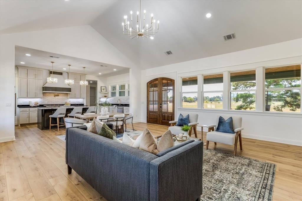 242 Private Road Mount Pleasant, TX 75455 - Photo 11 of 40 Vaulted ceiling with a chandelier, wood-finish flooring, kitchen island with counter seating, exposed wood double doors, and a wall of windows