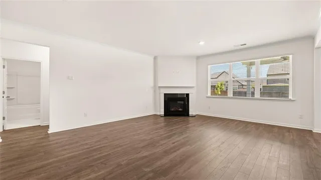 a view of an empty room with wooden floor fireplace and a window