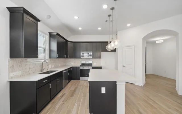 a large kitchen with stainless steel appliances kitchen island granite countertop a large kitchen island a stove a sink a refrigerator and a dining table with wooden floor