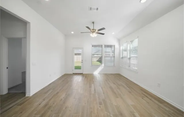 an empty room with wooden floor chandelier fan and windows