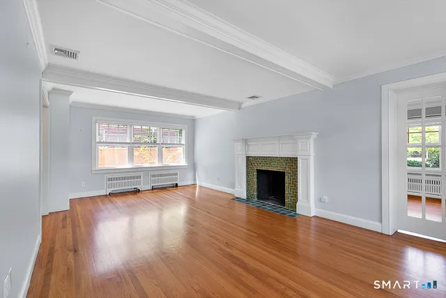 an empty room with wooden floor fireplace and windows