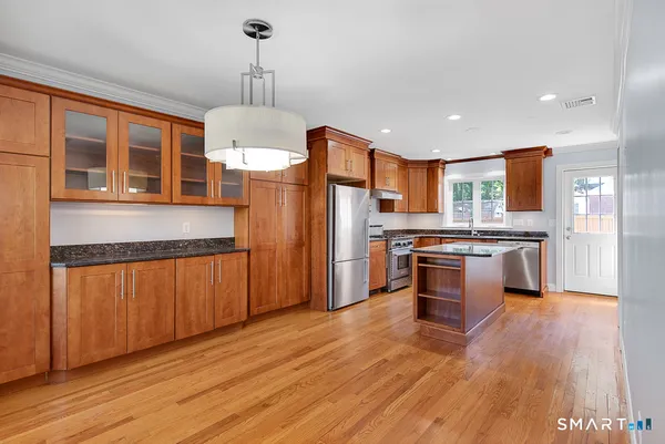 a open kitchen with stainless steel appliances granite countertop a refrigerator a stove and a wooden floors