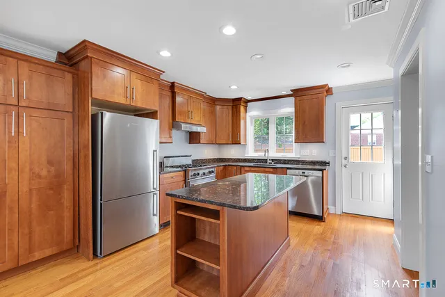 a kitchen with stainless steel appliances granite countertop a refrigerator a sink and a stove with wooden floor