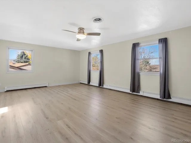an empty room with wooden floor chandelier fan and windows