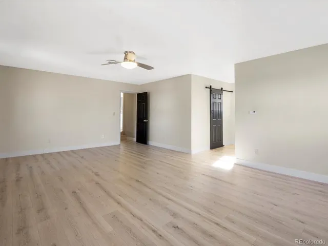 a view of an empty room with wooden floor and a ceiling fan