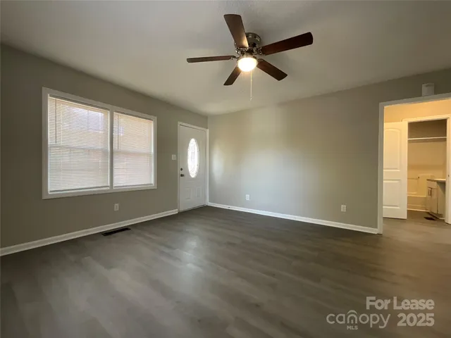 an empty room with wooden floor fan and windows