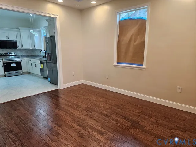 an empty room with wooden floor kitchen view and a window