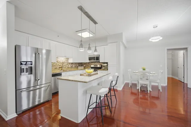 a kitchen with stainless steel appliances a refrigerator a stove a dining table and chairs with wooden floor