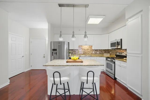 a kitchen with stainless steel appliances granite countertop a dining table chairs refrigerator and microwave