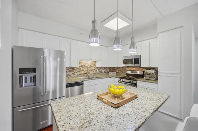 a kitchen with stainless steel appliances granite countertop a refrigerator a stove oven a sink dishwasher and white cabinets with wooden floor