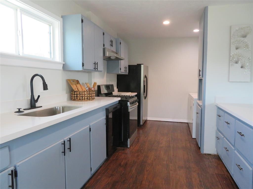 a kitchen with stainless steel appliances a sink dishwasher a refrigerator and wooden cabinets with wooden floor