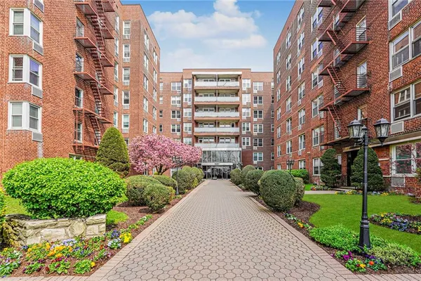 a front view of a multi story residential apartment building with yard and bench