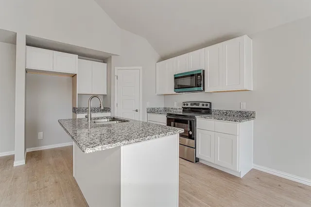 a kitchen with stainless steel appliances granite countertop a stove top oven a sink a refrigerator and white cabinets with wooden floor