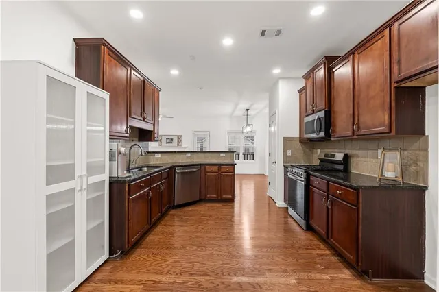 a kitchen with stainless steel appliances granite countertop wooden cabinets a stove top oven a sink and dishwasher a oven with wooden floor