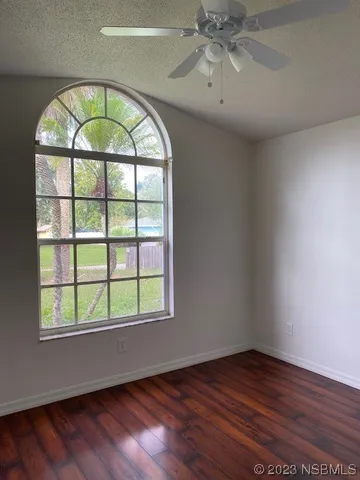 an empty room with wooden floor chandelier fan and windows