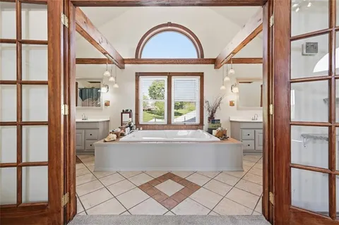 a bathroom with a tub a double vanity sink a window and mirror