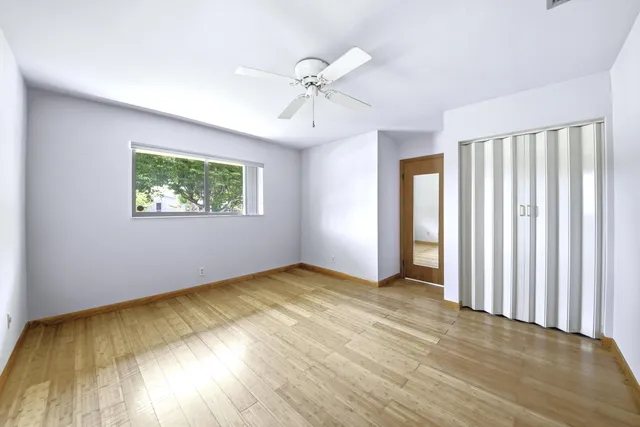 an empty room with wooden floor chandelier fan and windows