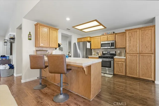 a kitchen with stainless steel appliances granite countertop a refrigerator a stove a sink a dining table and chairs with wooden floor