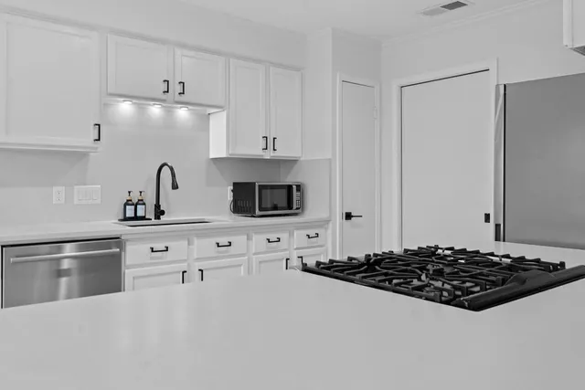 a kitchen with stainless steel appliances a stove a sink and white cabinets