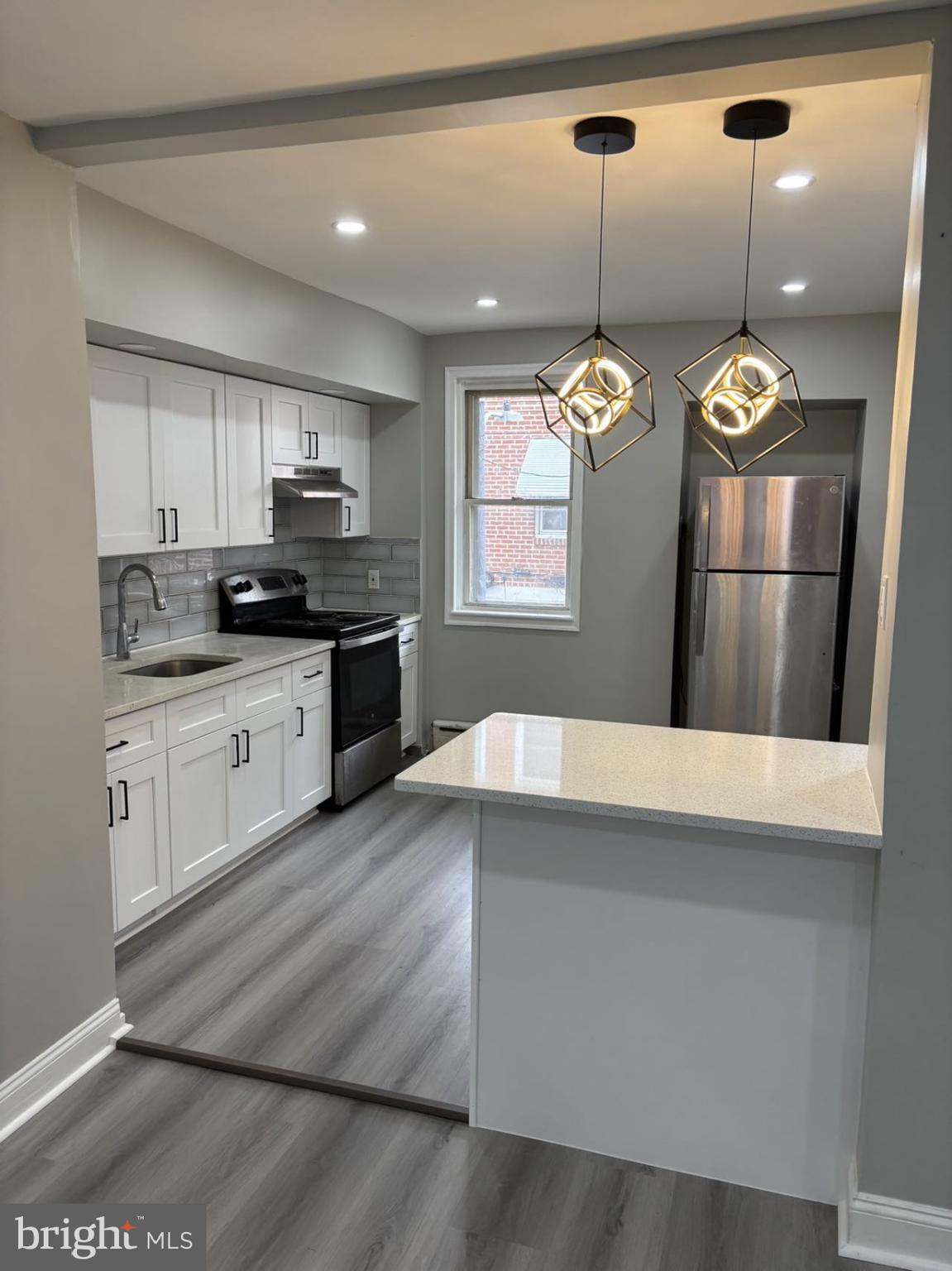 4007 Higbee Street Philadelphia, PA 19135 - Photo 20 of 20 a kitchen with kitchen island granite countertop a stove a sink and white cabinets with wooden floor