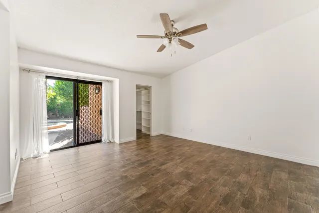an empty room with wooden floor fan and windows