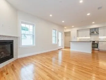 a view of an empty room and kitchen with wooden floor