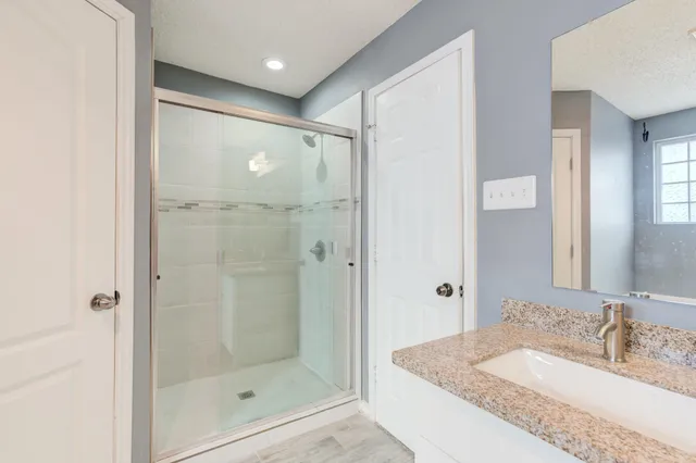 a bathroom with a granite countertop sink a mirror a glass door and shower
