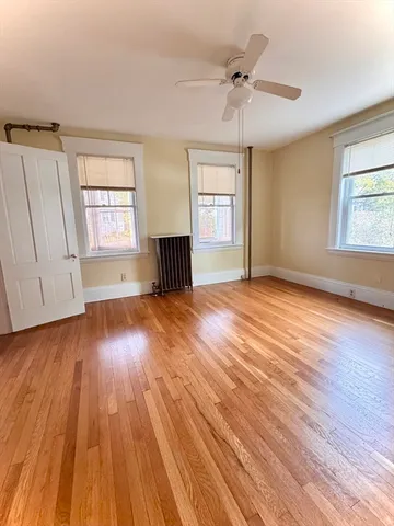 an empty room with wooden floor chandelier fan and windows