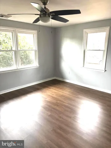 an empty room with wooden floor windows and fan