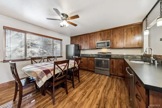 a kitchen with stainless steel appliances granite countertop a stove top oven a sink dishwasher a dining table and chairs with wooden floor