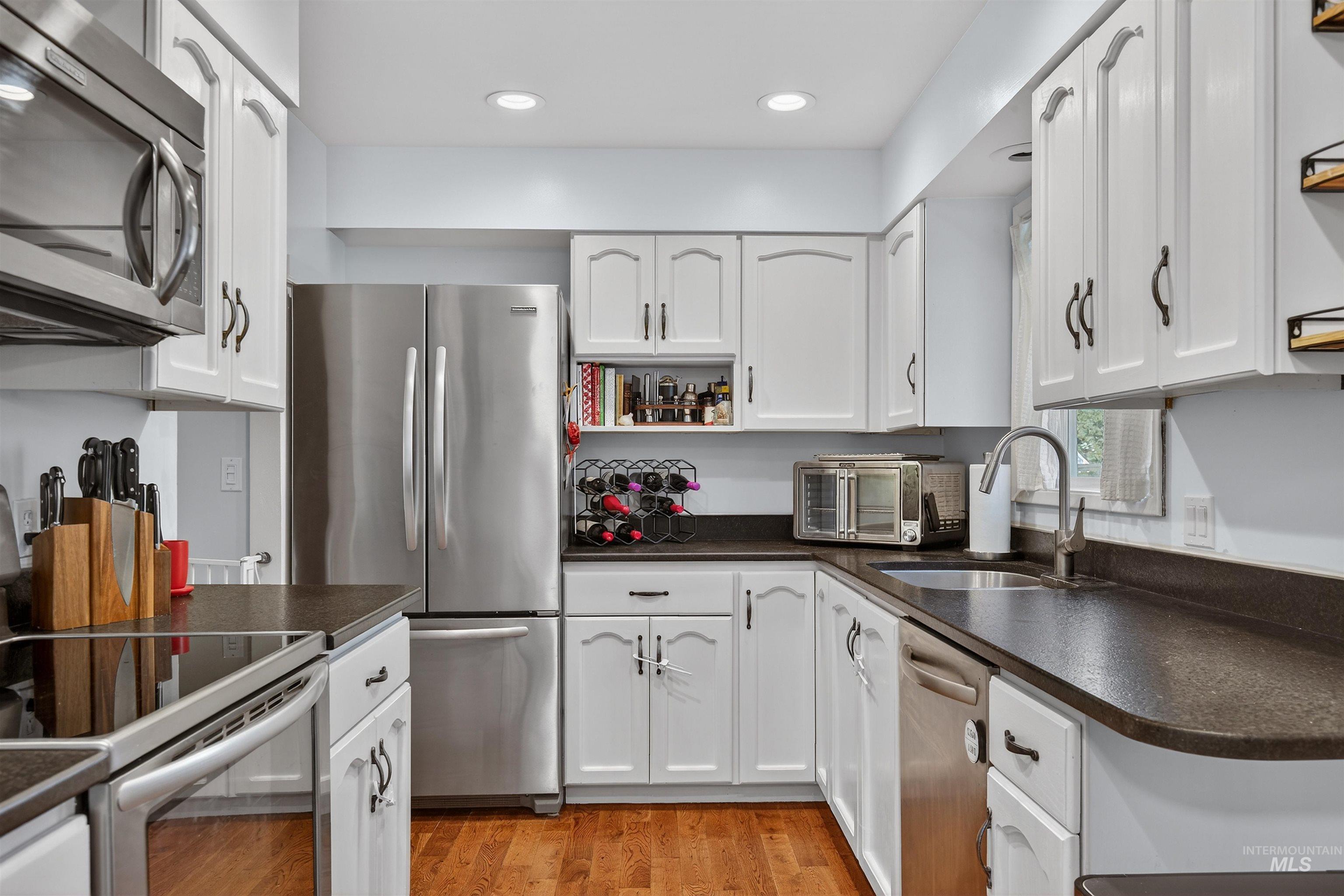 209 Walnut Drive Potlatch, ID 83855 - Photo 6 of 27 Kitchen with dark countertops, open shelves, stainless steel appliances, white cabinets, and light wood finished floors