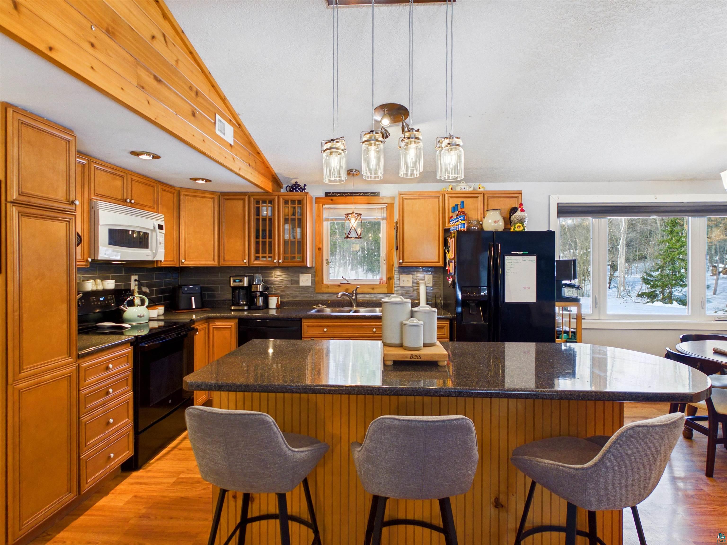 10719 North Oak Ridge Street Hayward, WI 54843 - Photo 15 of 57 Kitchen featuring a center island, black appliances, a kitchen breakfast bar, pendant lighting, and dark stone counters