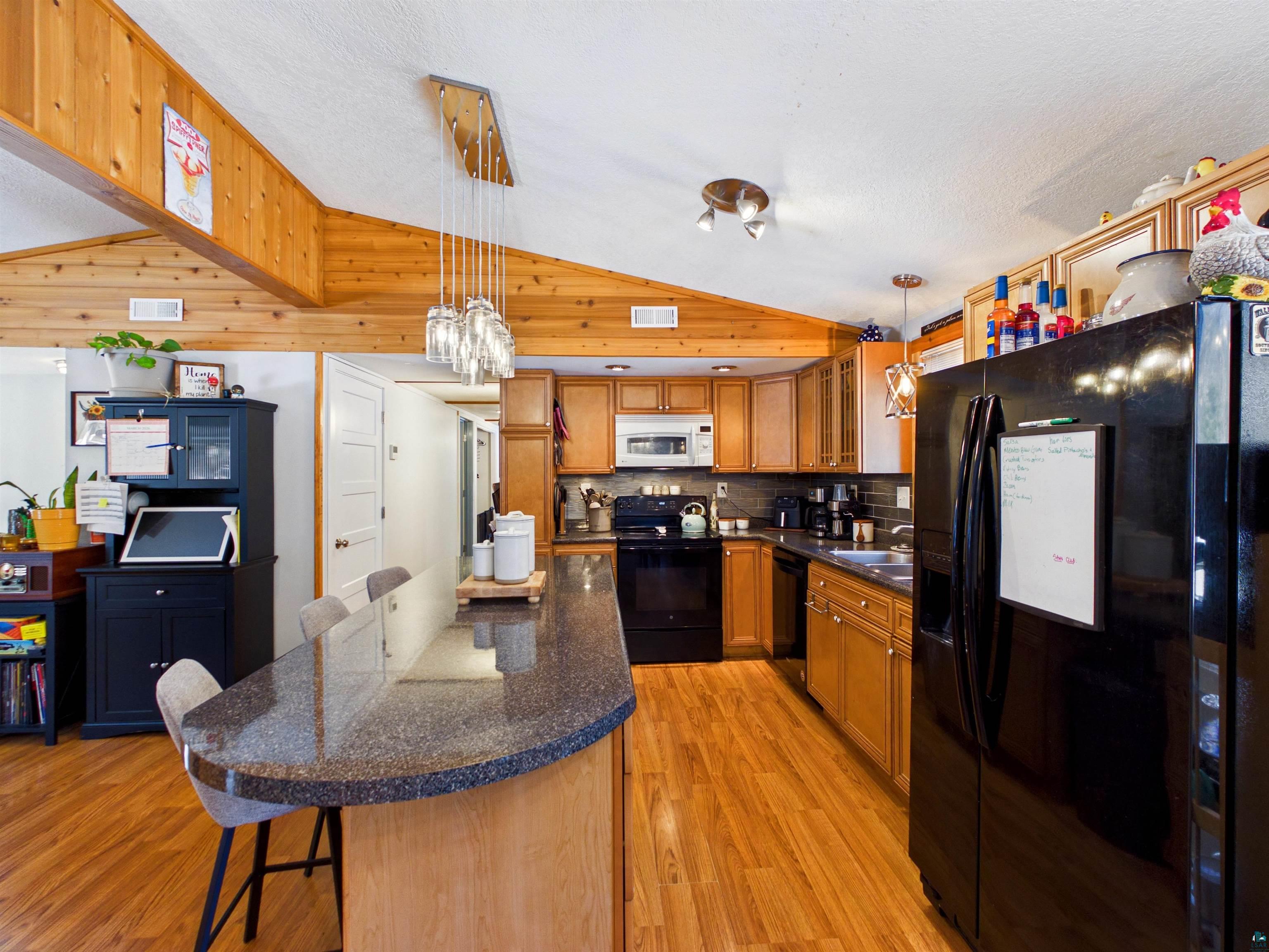 10719 North Oak Ridge Street Hayward, WI 54843 - Photo 17 of 57 Kitchen with black appliances, a breakfast bar, a kitchen island, light wood-style floors, and backsplash