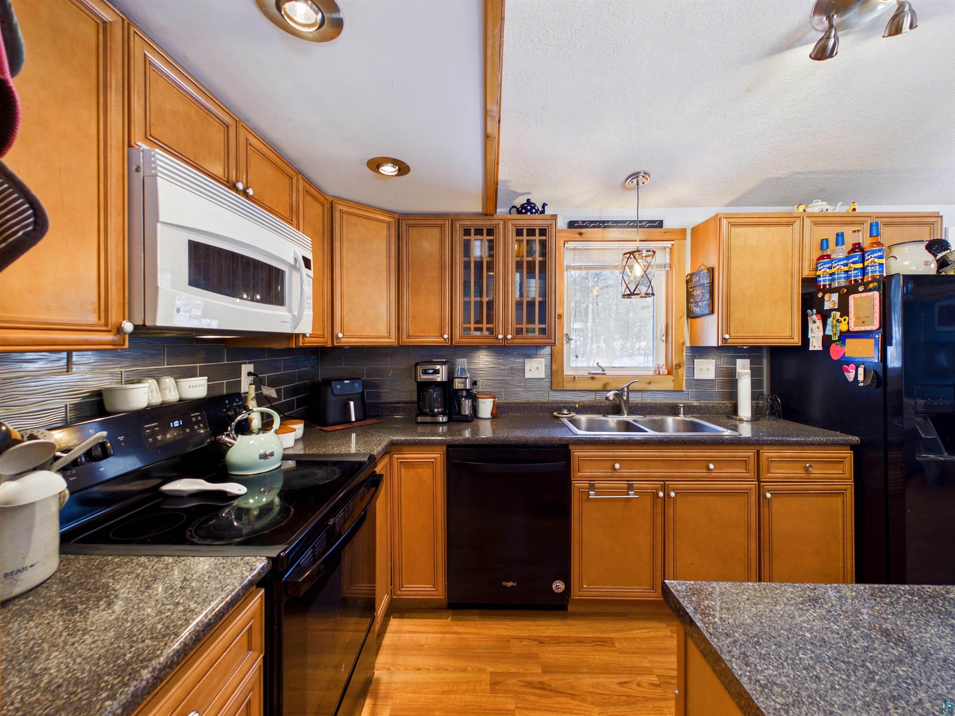 10719 North Oak Ridge Street Hayward, WI 54843 - Photo 19 of 57 Kitchen with black appliances, wood finish cabinets, glass insert cabinets, hanging light fixtures, and light wood-style floors