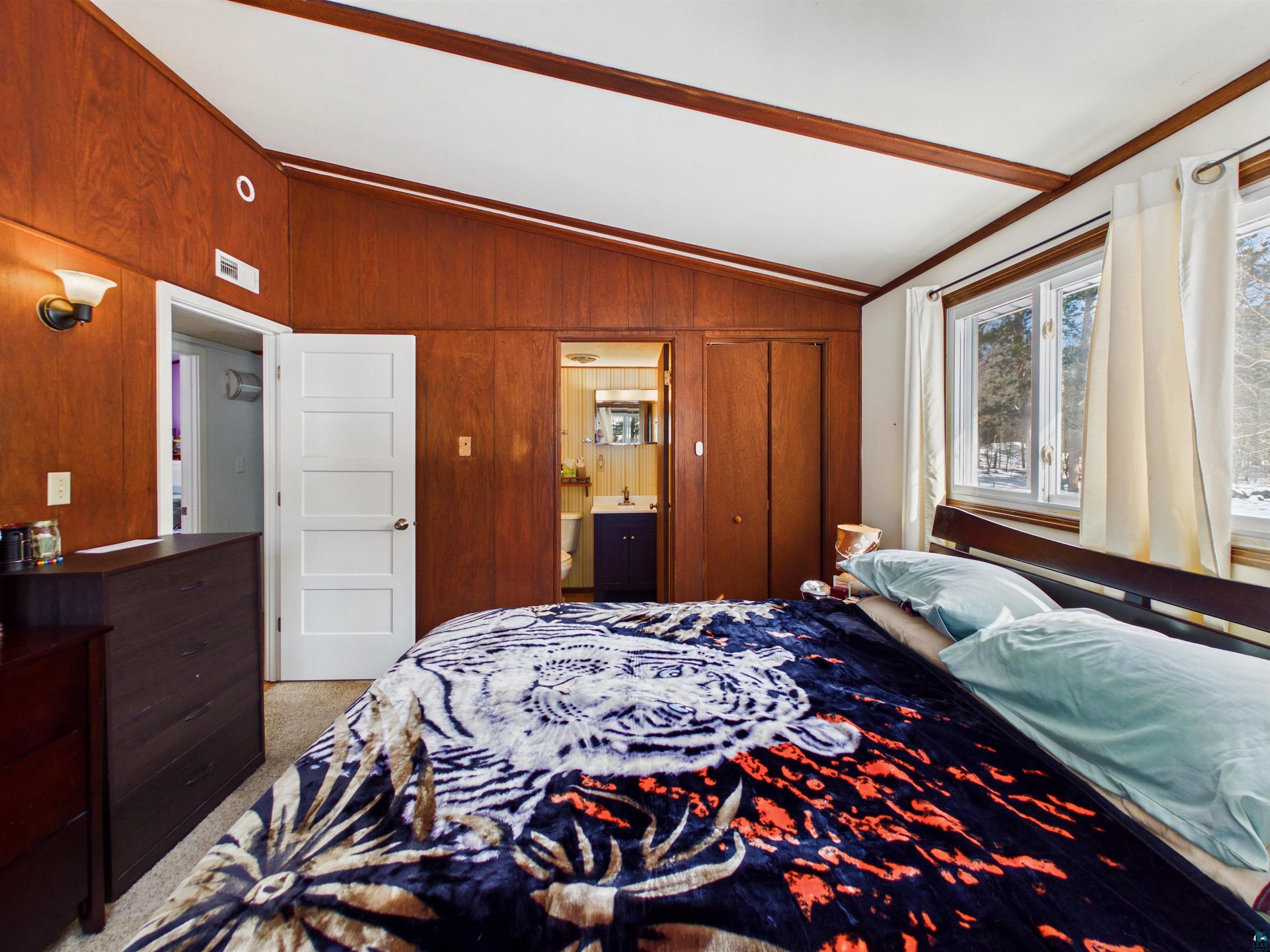 10719 North Oak Ridge Street Hayward, WI 54843 - Photo 32 of 57 Bedroom featuring vaulted ceiling, connected bathroom, light colored carpet, and wood walls