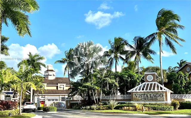 a front view of a building with lot of trees and cars