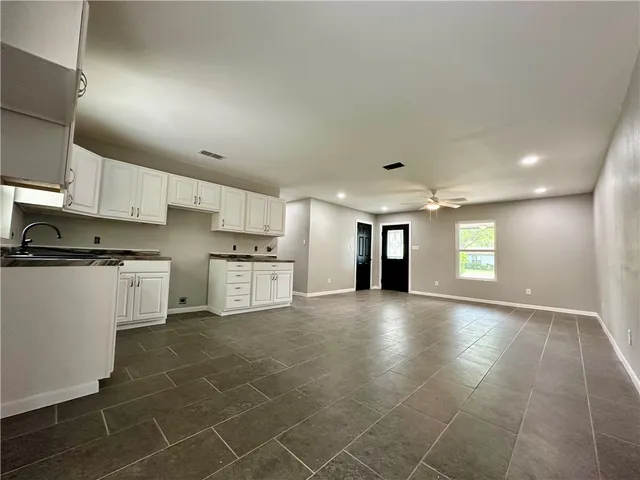 a view of an empty room with kitchen and window