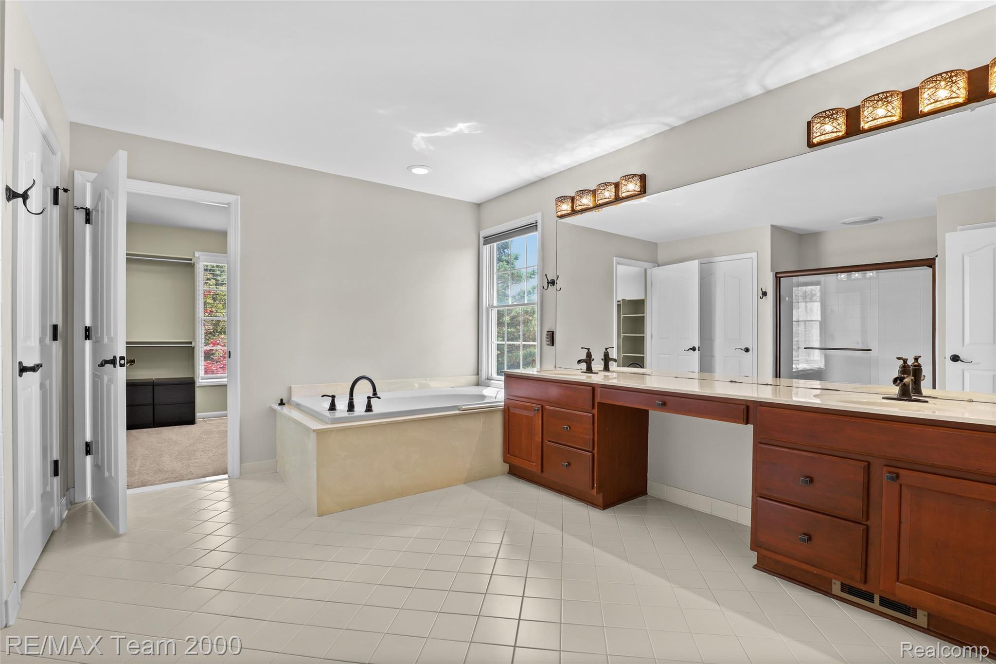 1248 Lasalle Road Canton, MI 48187 - Photo 56 of 67 Bathroom featuring dual wood-finish vanities with light countertops, a built-in garden tub, a large wall mirror, and white tile flooring