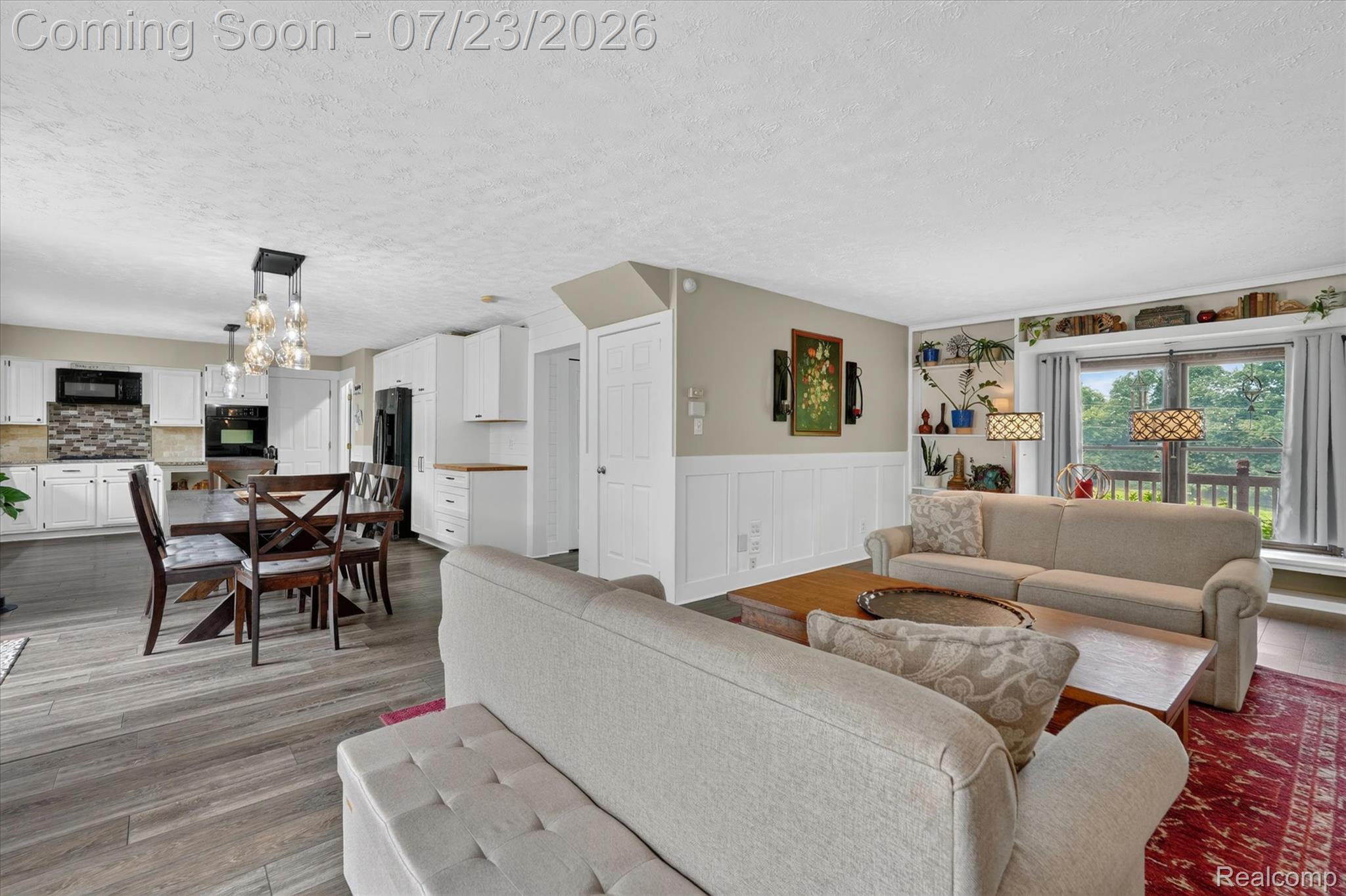 2795 Bird Road Ortonville, MI 48462 - Photo 11 of 62 Open-concept living area with wood-finish flooring, a contemporary dining chandelier, white cabinetry, integrated appliances, and a full-light glass door leading to an outdoor space